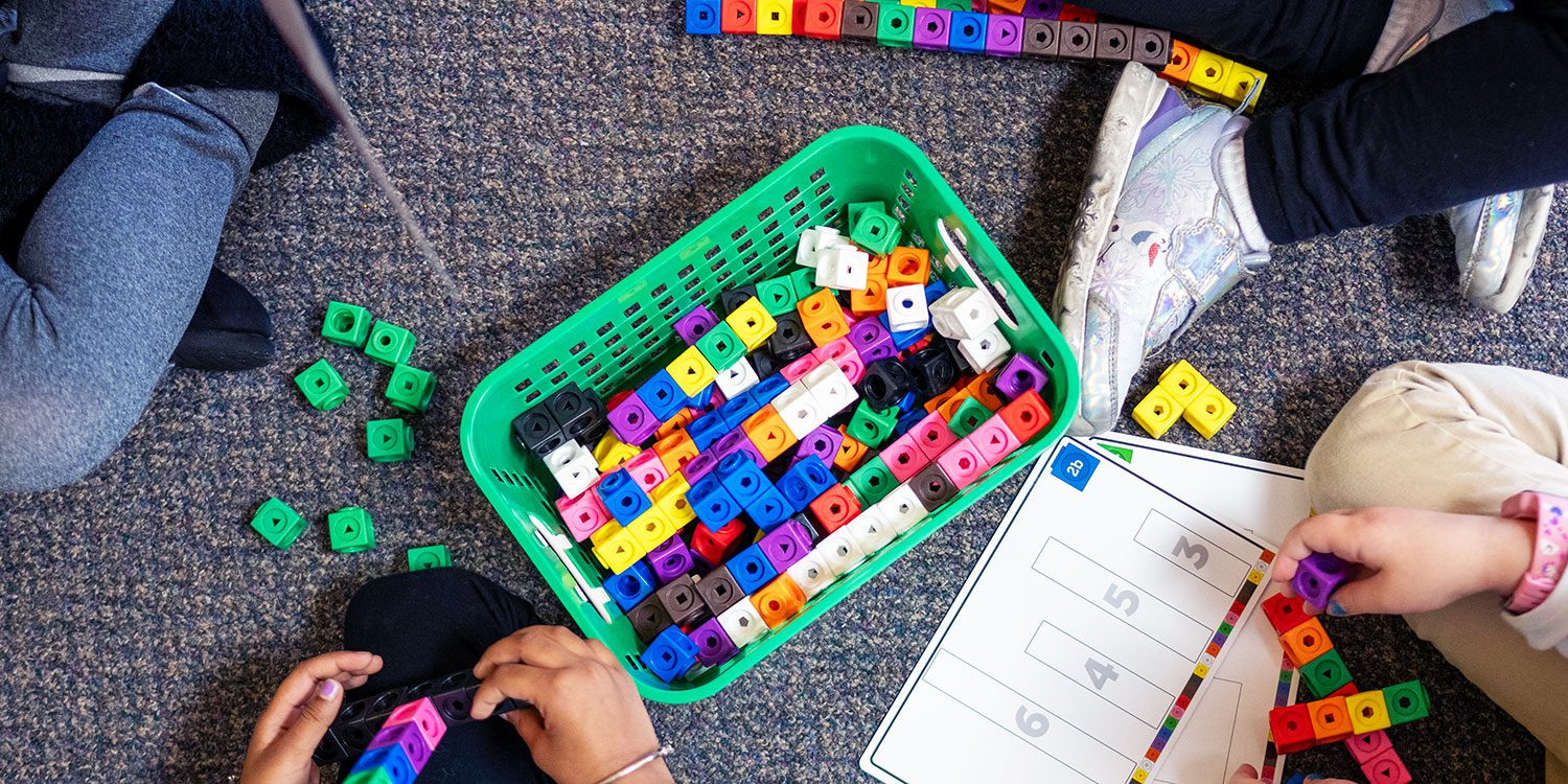 Students building with colorful connecting cubes on a classroom carpet.